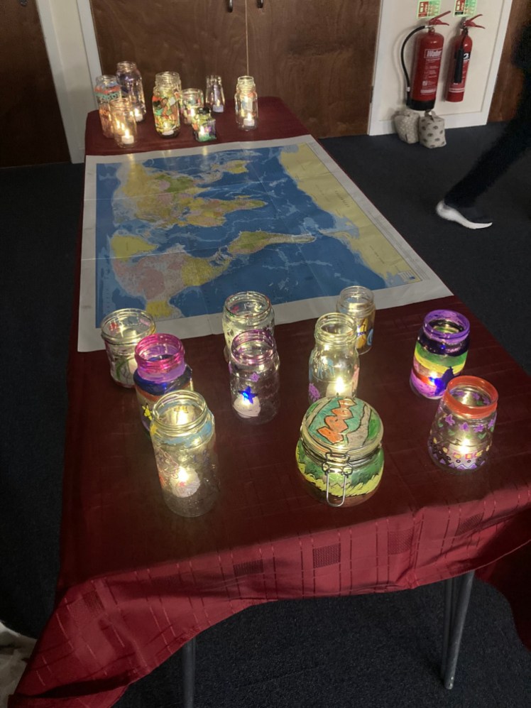 A table covered with a red tablecloth and a world map. On each side of the world map are jars the Brownies have decorated with a battery-operated tealight twinkling inside.