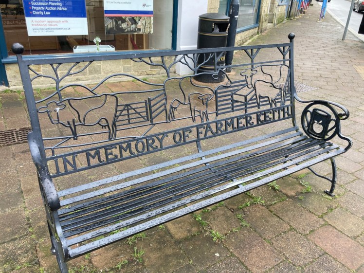 A wrought iron (well, probably steel but you can picture it better if I call it wrought iron) bench where the entire back is a farm scene with several cows and the words "In memory of Farmer Keith" along the bottom.