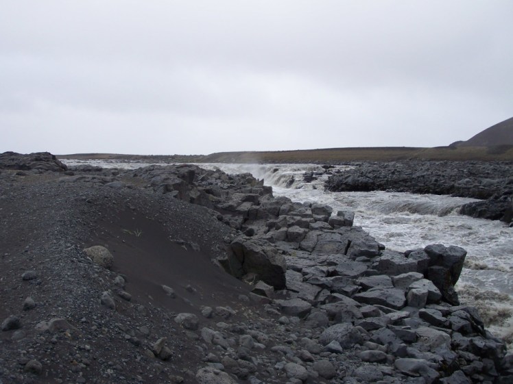 A very grey and rough river full of glacial debris, running through a grey rocky landscape. We sat near here for quite some time.