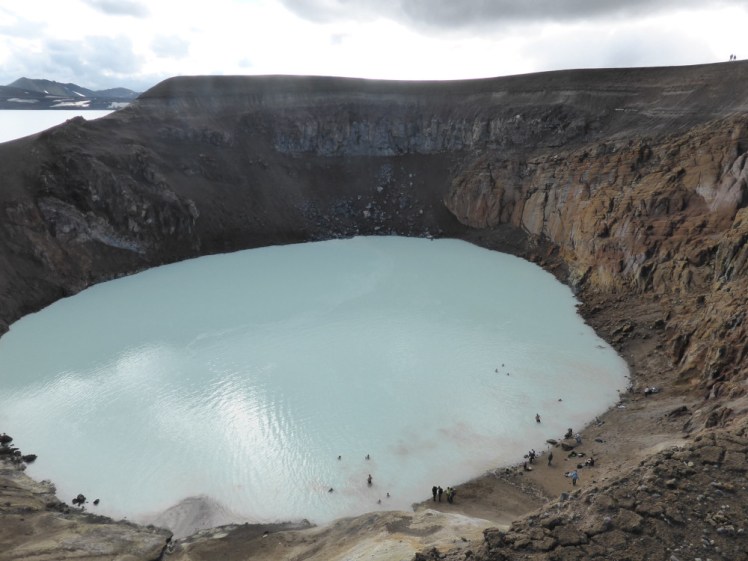 People swimming in Viti, dragging mud from the shore into the milky blue water. The photo is taken from the rim of the crater, looking almost straight down from the north side.