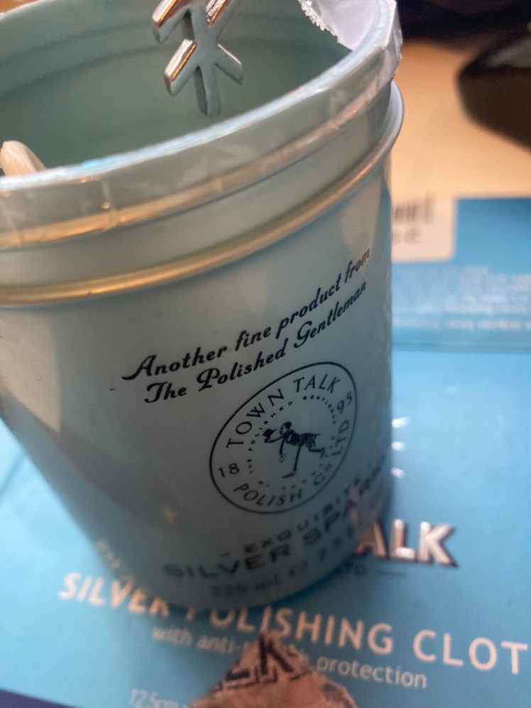 A blue pot of silver polishing solution with my rune hanging over it (but not actually dropped in because I can't be bothered to get up and rinse and dry it right now).