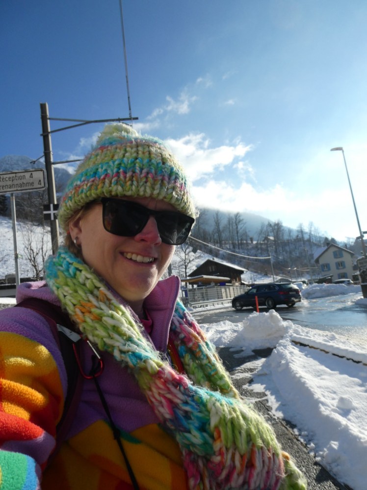 A selfie in a great hat and scarf and very colourful fleece against a background of white snow and vivid blue sky.