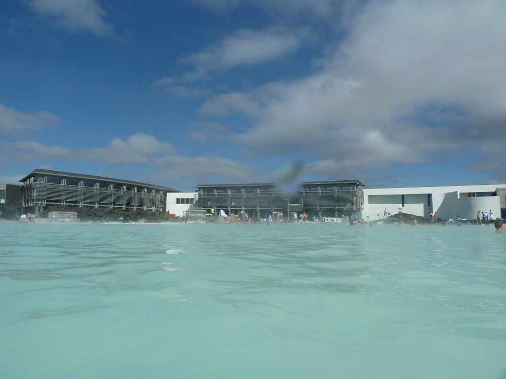 The Blue Lagoon in summer, looking across the water to the building. There are lots of people in the water near the building but there's an expanse of empty water between me and them, showing how much of the lagoon isn't crowded, even on a busy summer day.