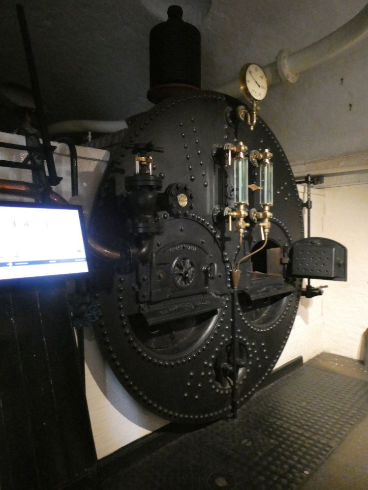 The front of one of the three giant boilers in the engine room, a big black thing with glass and brass valves and two small doors where you shovel the coal in.