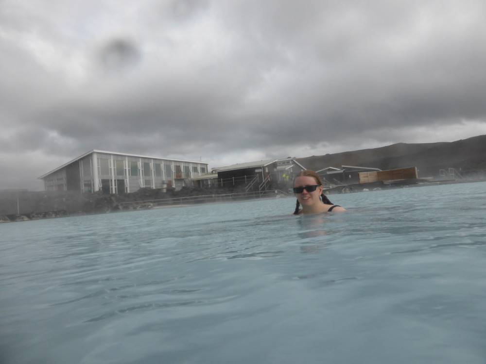 A timer selfie in front of the old facility building, with the orange-streaked mountain behind it.