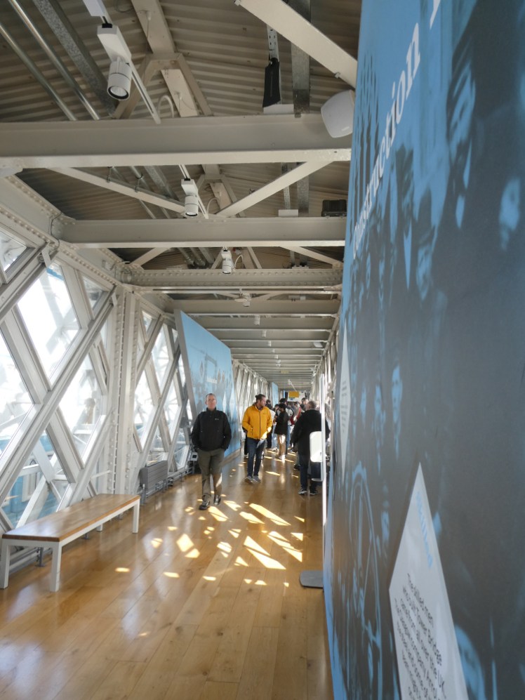 The East Walkway, a glass walkway supported by white metal tubes and with blue information panels all along the inside.