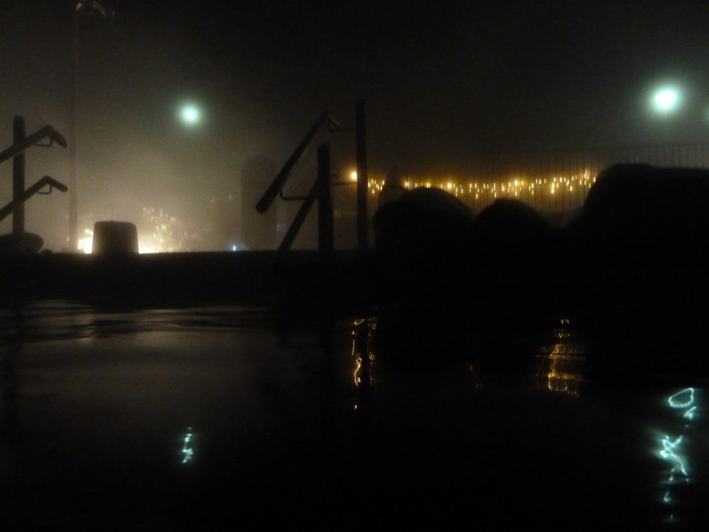 Fontana by night. I think I'm in the natural pool but it's hard to tell when it's so dark. A set of stairs into a pool is silhouetted by a light and there's a string of fairy lights hanging up on the right.