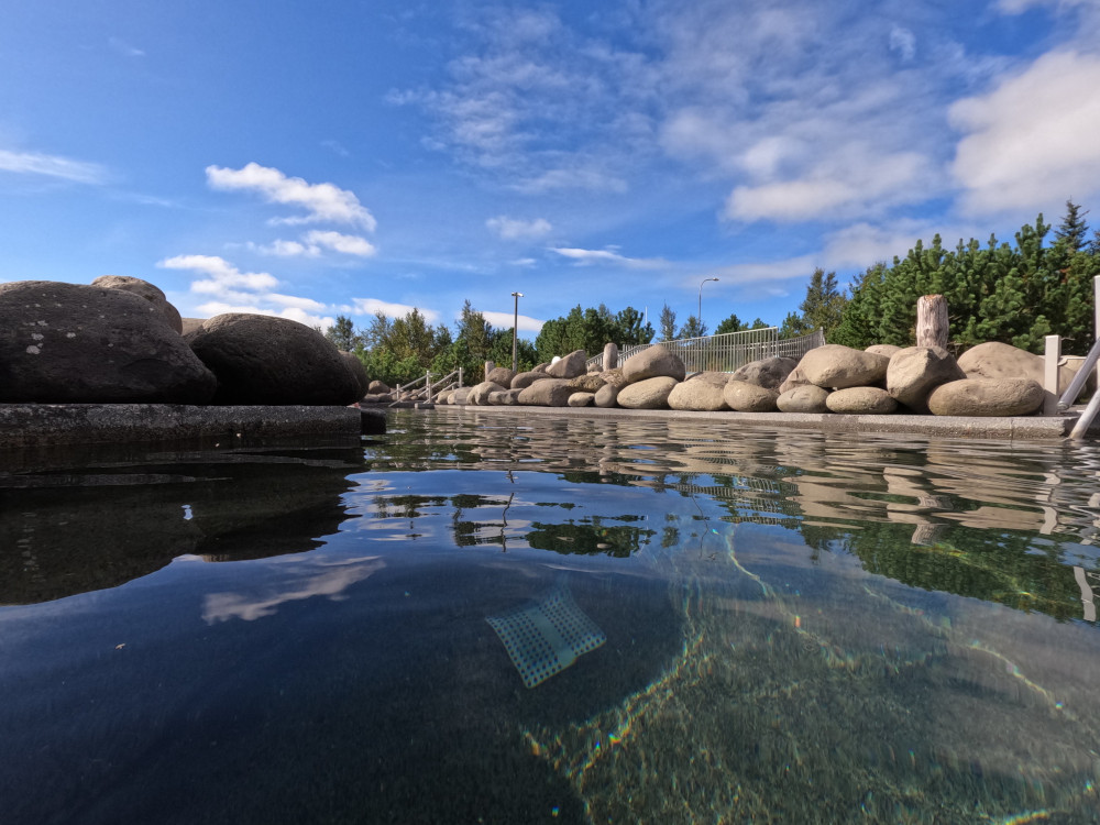 Fontana's natural lava pool in such bright sunshine that the blue sky is reflecting off the dark water.