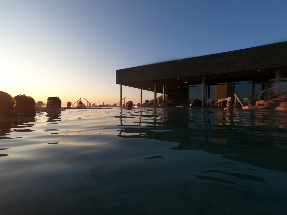The sun setting over the pool and almost silhouetting the building over the pool.