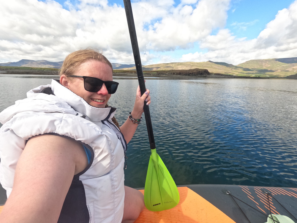 A selfie on a paddleboard wearing a ludicrous padded gilet-style buoyancy aid and holding a paddle with a lime green blade.