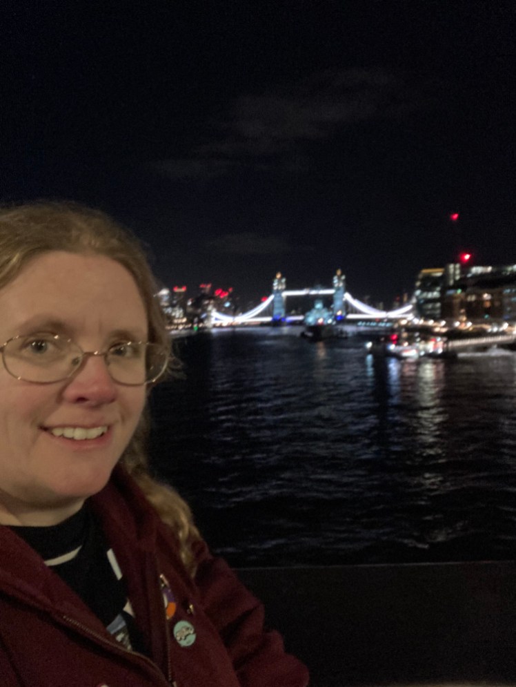 A selfie with Tower Bridge illuminated in the background by night.