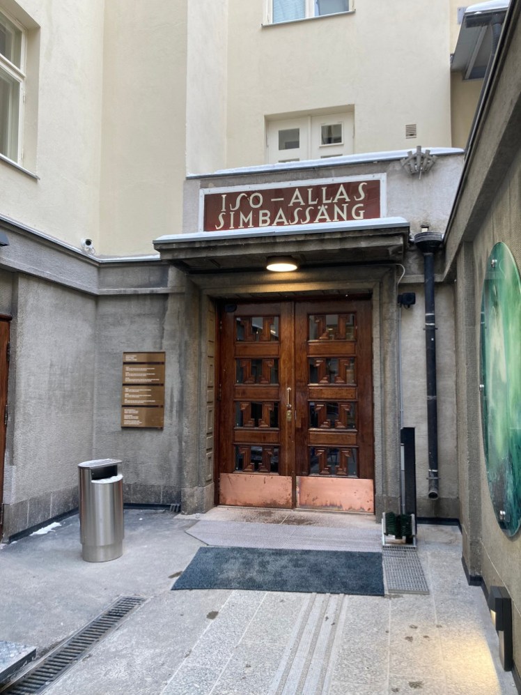 A fairly imposing pair of double wooden doors at the end of the corridor right in that corner, with the words "(big) swimming pool" over them in Finnish and Swedish.