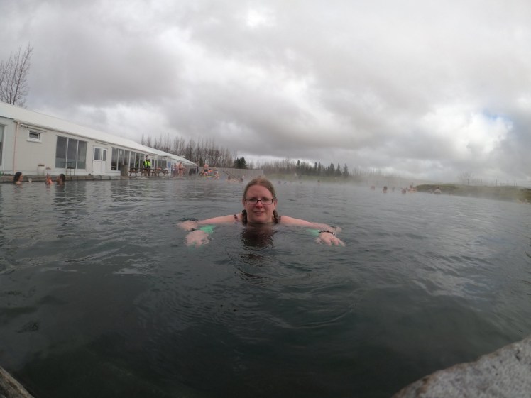 A timer selfie in the Secret Lagoon, hanging over a foam pool noodle in the water and looking straight at the camera.