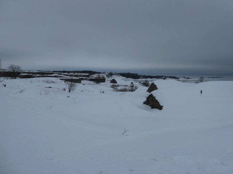 What looks like a featureless field of snow is actually thick snow burying several rounded grass-covered bunkers and fortress walls.