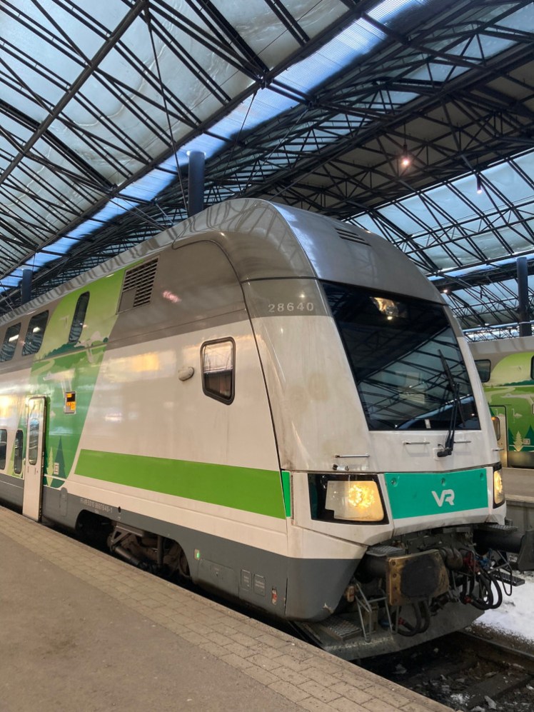 The double-decker train, in white with green stripes and a grey top, parked at Helsinki Central.