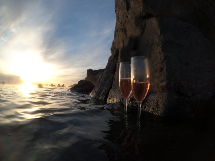 Two glasses of pinky-orange wine on a ledge next to the "cliff" in the Sky Lagoon. Over on the infinity edge, the sun is getting low.