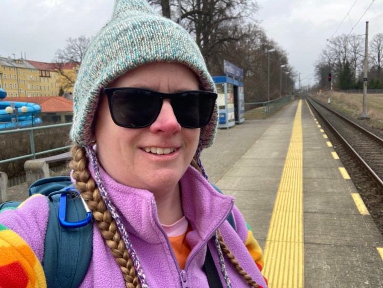 A selfie on the platform at Františkovy Lázně Aquaforum station. I'm wearing sunglasses, my pointed hat turned to show the green side and my rainbow fleece, although you can mostly only see the purple collar and shoulders from here.