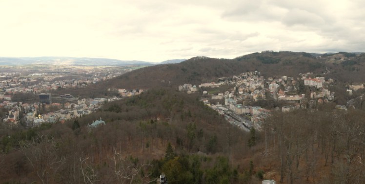 The view over Karlovy Vary from the Diana lookout tower. The town is scattered over the hills below with the main spa area stretching roughly across the centre of the picture and partly blocked by the hump-shaped hill in the middle.