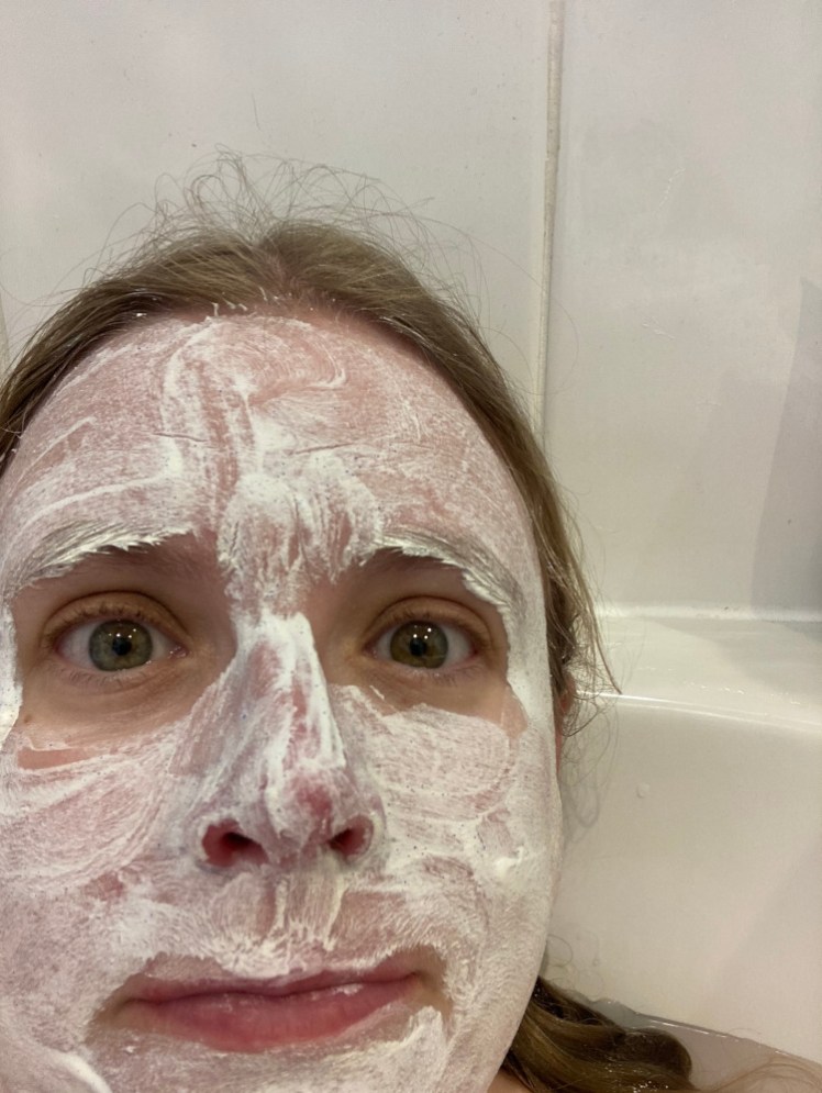 Me in the bath at home with a white clay mask all over my face.
