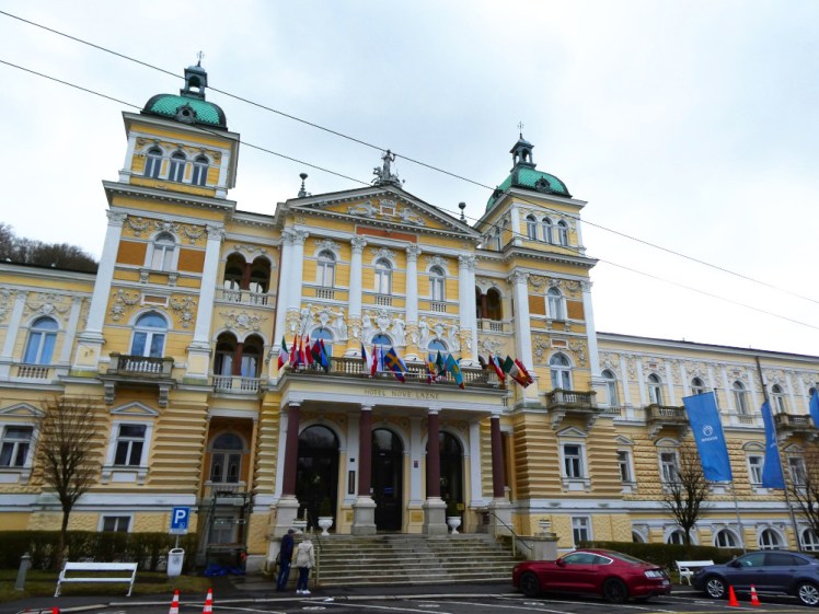 Hotel Nové Lázně, a yellow and white Neo-Renaissance palace of a hotel, with towers and columns and a lot of flags.
