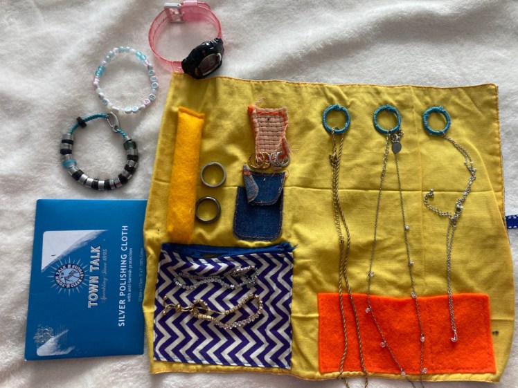 A blue and yellow jewellery roll with assorted waterproof jewellery in it.