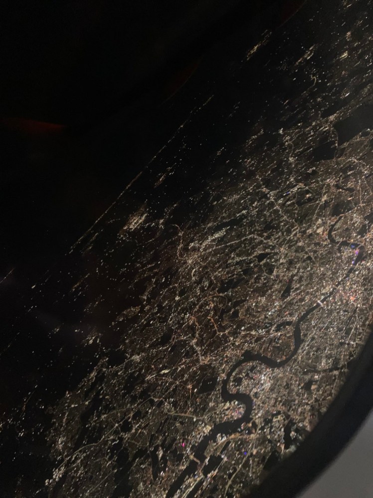 London by night seen (at quite a dramatic angle) from a plane flying over the north side of the Thames.