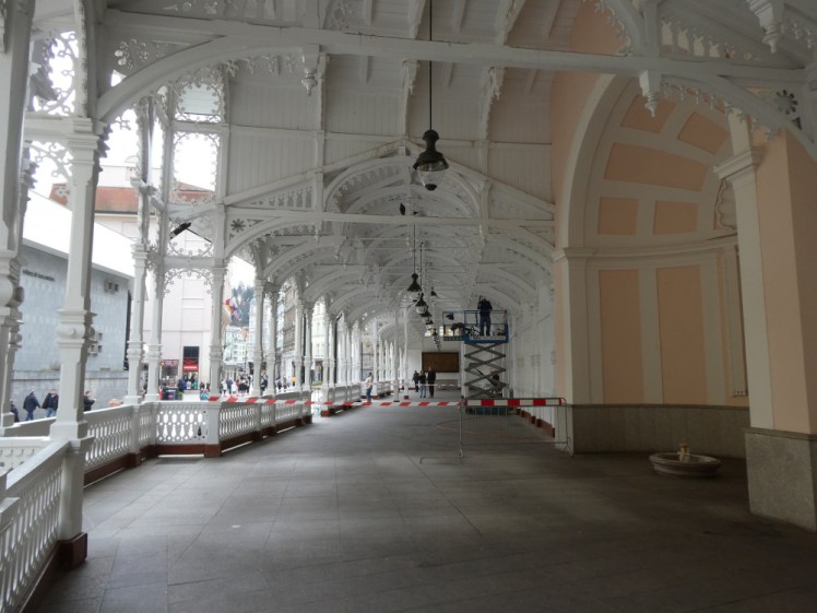 Inside the Market Colonnade which is all white wooden lace. Part of it is taped off with red and white tape and behind it, a man in a scissor lift is doing some maintenance to the ceiling.