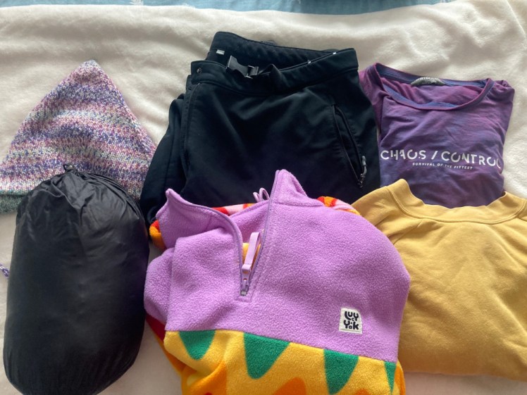 The clothes that I'm wearing: a purple pointed knitted hat, my black down jacket, black lined hiking trousers, a purple t-shirt, yellow sweatshirt and my big rainbow and purple fleece.