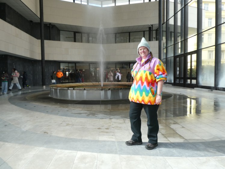Me with the 72° Vřídlo hot spring which erupts like a 12m fountain into a glass cupola above its own glass and concrete pavilion.