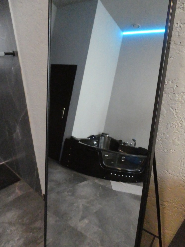 A shiny black corner jacuzzi bath reflected in a full-length mirror.