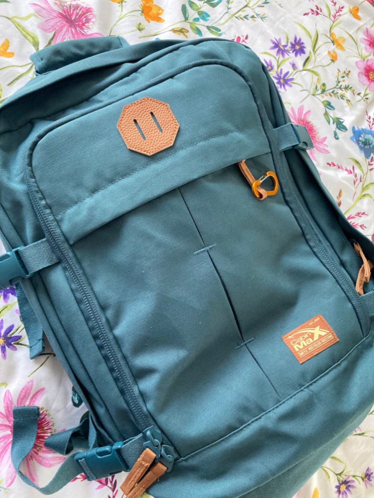 The Cabin Max Metz 30l cabin backpack in teal laid out on a flowery bed to show the pockets on the front and overall what it looks like.