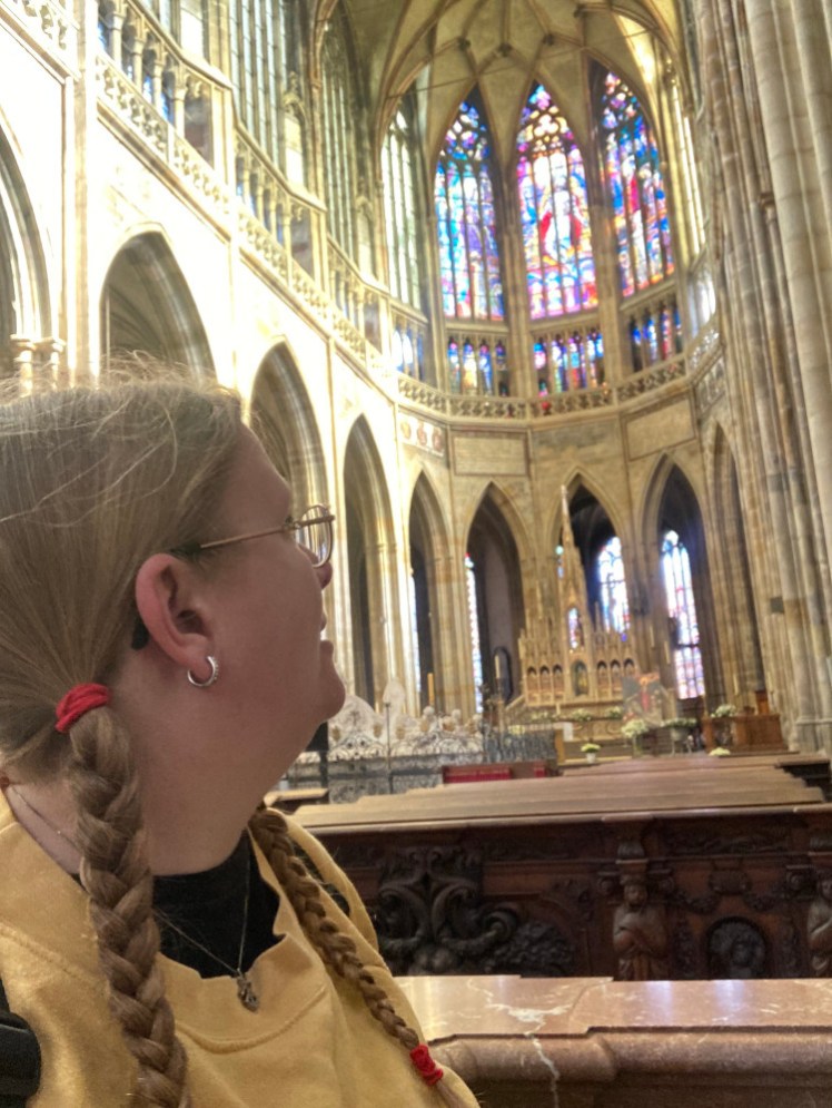 Me, in a yellow jumper, in the cathedral, my head turned to look at the half-circle of stained glass over the altar.