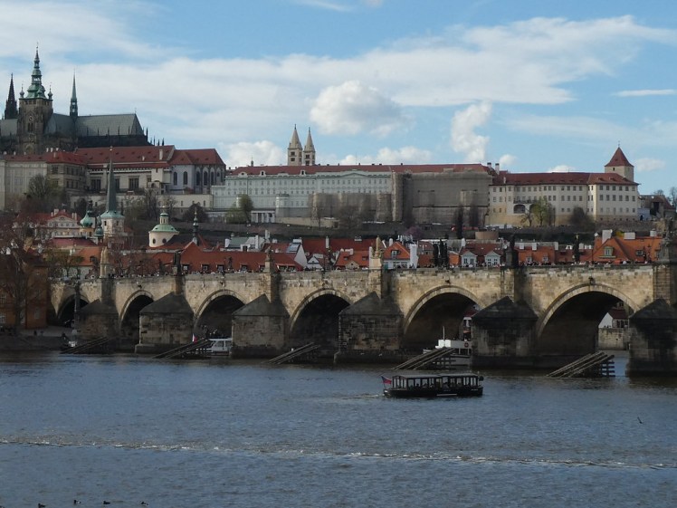 Charles Bridge up close seen from the eastern side of the river with lots of people on it and the castle in the background.