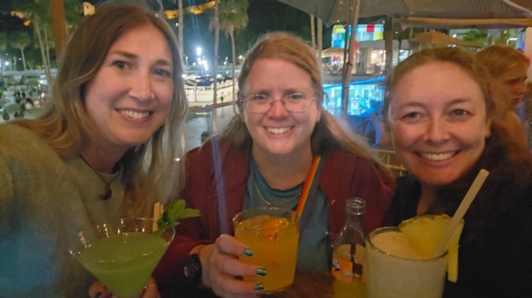 The three of us having drinks in a bar by the harbour. Catherine has a bright green drink, Esther has a pina colada and I've got a Fanta in a glass with ice and a slice.