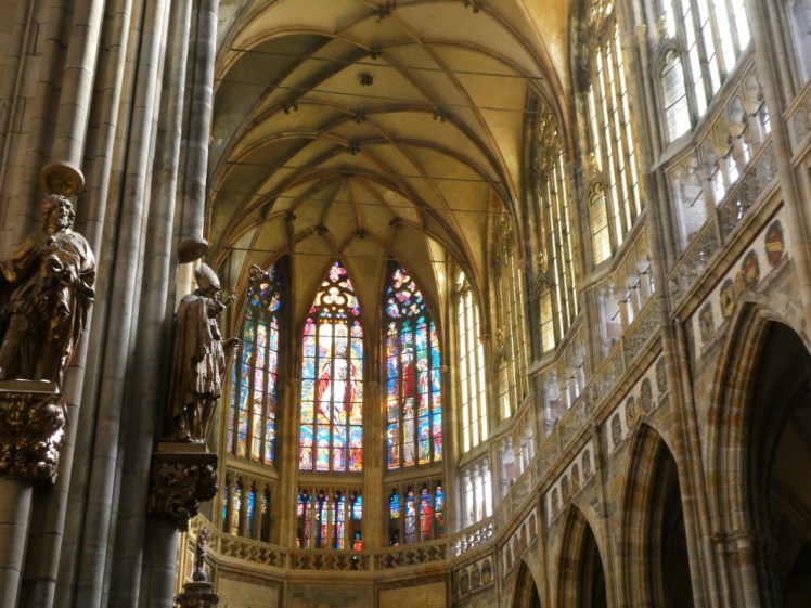 The east end of the cathedral, above the altar. In the foreground is a pillar with figures mounted on it, you can see arches and double height windows and vaulted ceiling and at the end are three tall windows arranged around the rounded end of the quire.