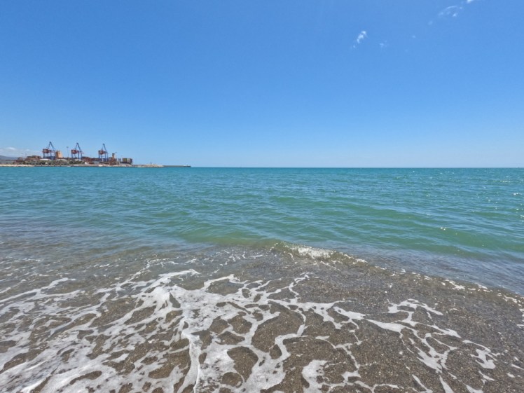 The Mediterranean, a perfect turquoise teal under a blue sky, with the cranes of Malaga port sticking out into it to the left.