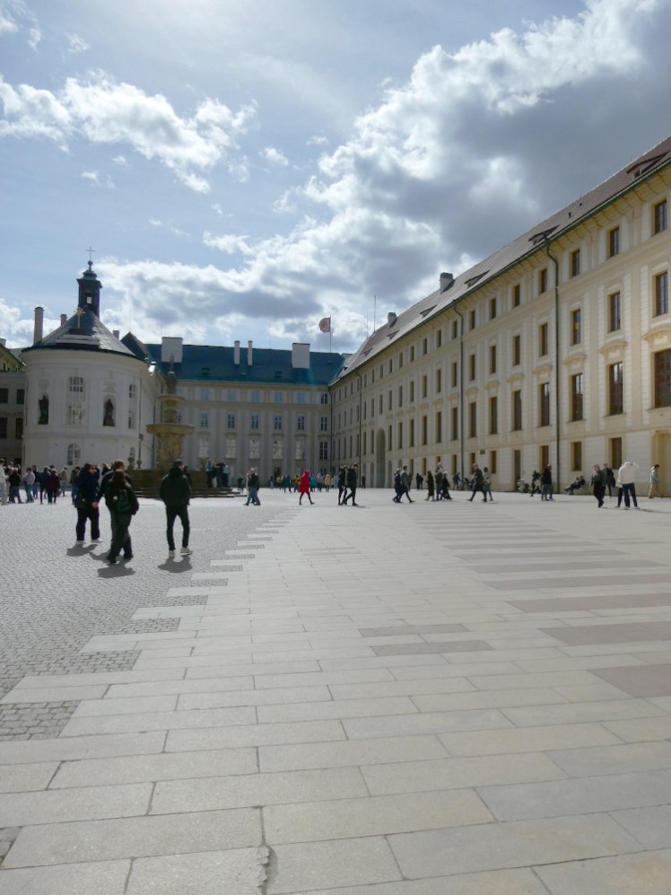 One of the inner courtyards of Prague Castle, with a yellowish building on the right and a small chapel on the left.