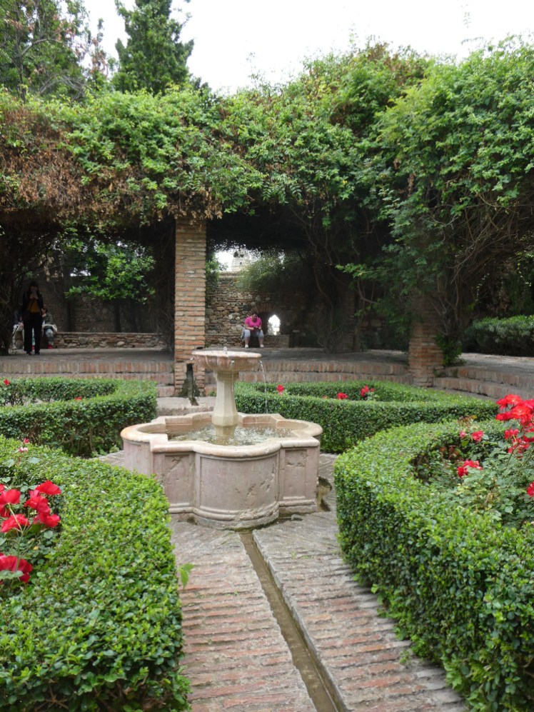 The garden, a square courtyard with walkways leading to a fountain in the middle. There was a pigeon drinking from it earlier but it's flown away by now.