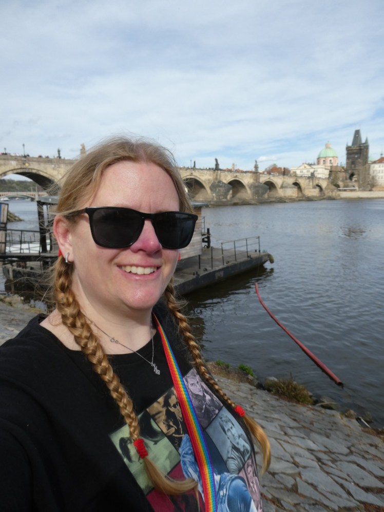 A selfie in an Eras Tour-style t-shirt showing pictures of Ethan Hunt in the Mission: Impossible film series. Behind me is Charles Bridge.