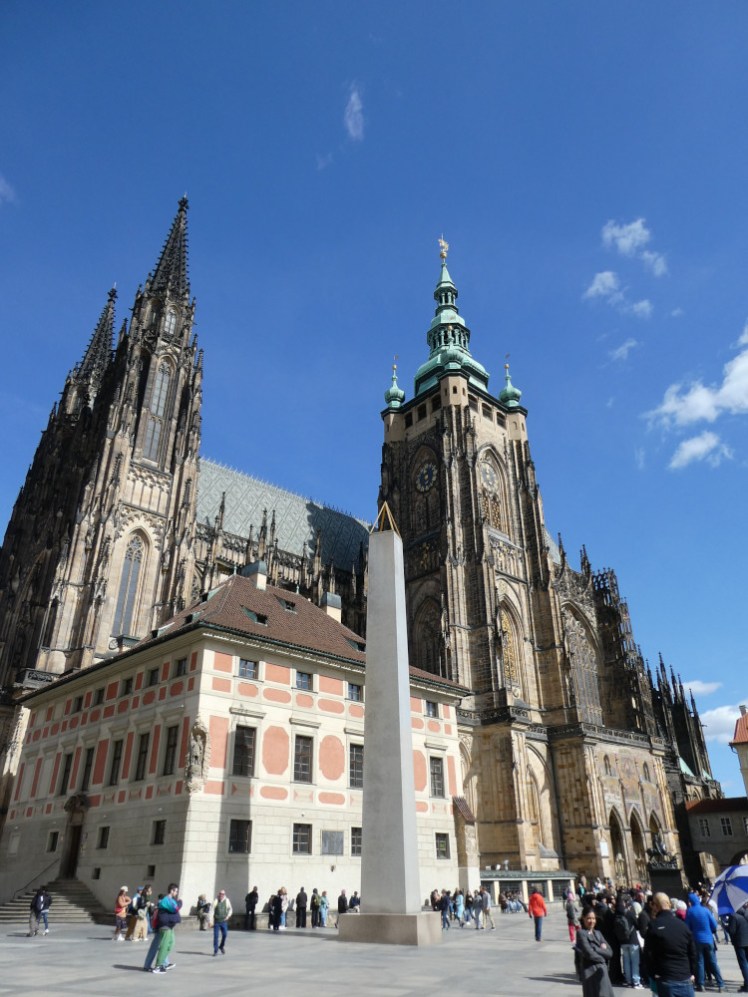 St Vitus Cathedral from outside, on the south side. It has an unusually tall tower halfway down the south side as well as two towers at the west end. It also has a building I can't identify, much more modern and much more plain although plastered in cream and pink, stuck into its corner.