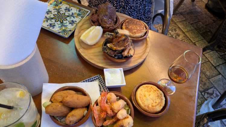 Two plates of tapas, which include a slab of beach, fried aubergine in honey, two egg potato tortillas, a dish of croquettes and prawns.
