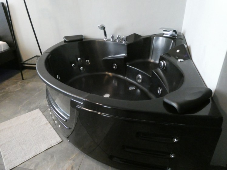 The bath, a shiny black corner bath with lots of knobs and jets and a "window" in the front.
