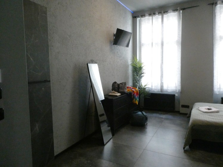 The room - it has high grey fake marble walls, thin light grey curtains, a black chest of drawers and a mirror and not a whole lot else.