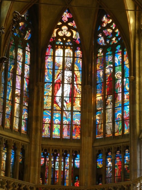 A triptych of tall windows in a more traditional style which I think show God holding Jesus's body after crucifixion. On the windows to the left and right are kings and saints in magnificent outfits looking up the scene.