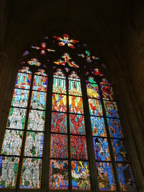 A modern stained glass window with what looks like flames up the middle section, saints in green and white on the left and saints in blue on the right.