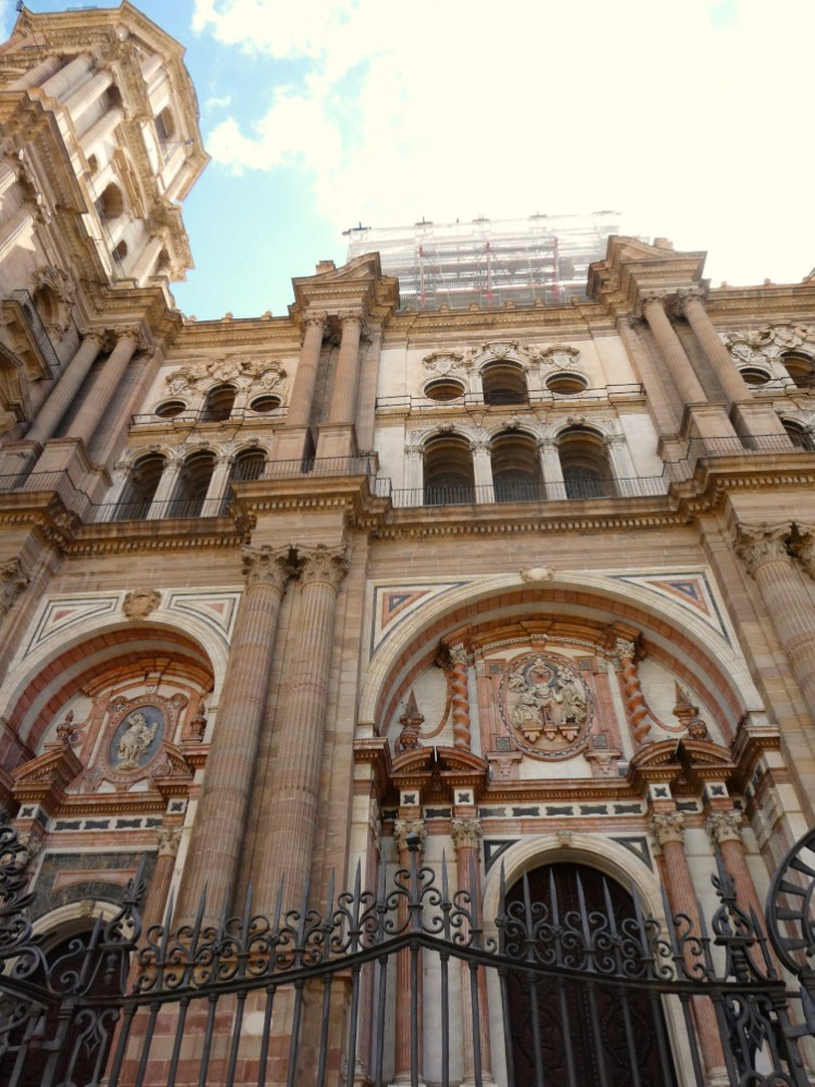 The Baroque facade of the cathedral, as seen from very close up and low down. There are ornate arches at ground level and two "storeys" higher up with pillars separating the frontage into three parts.