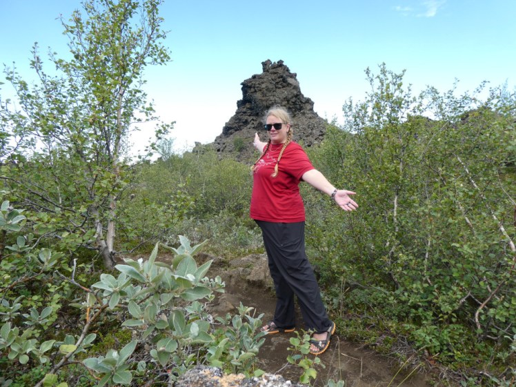 Me in a different lava field in Iceland, this one covered in short green trees. I'm wearing a red t-shirt and black trousers and trying to look vaguely triumphant with arms spread and wearing black and orange sandals.