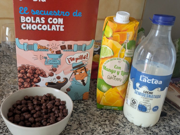 Breakfast at the apartment - a box of chocolate cereal with a bowl poured out, a carton of mango & lime juice and a bottle of milk.