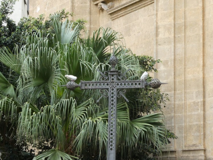 The garden to the north of the cathedral. There's a decorative metal cross with two white pigeons or doves perched on it like an omen.