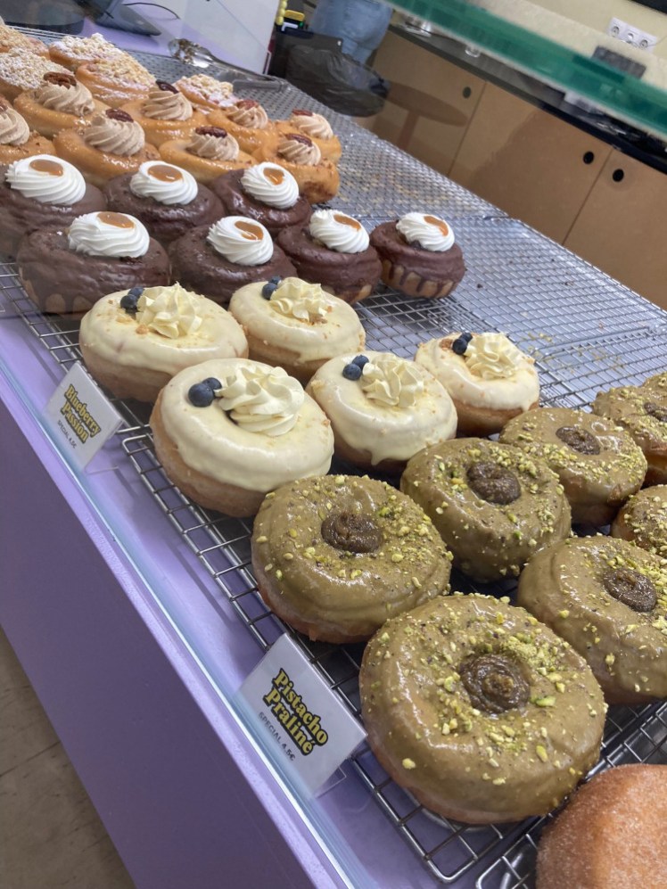 A counter of large doughnuts, mostly so covered in icing or cream or nuts that you can't actually see the doughnut underneath.
